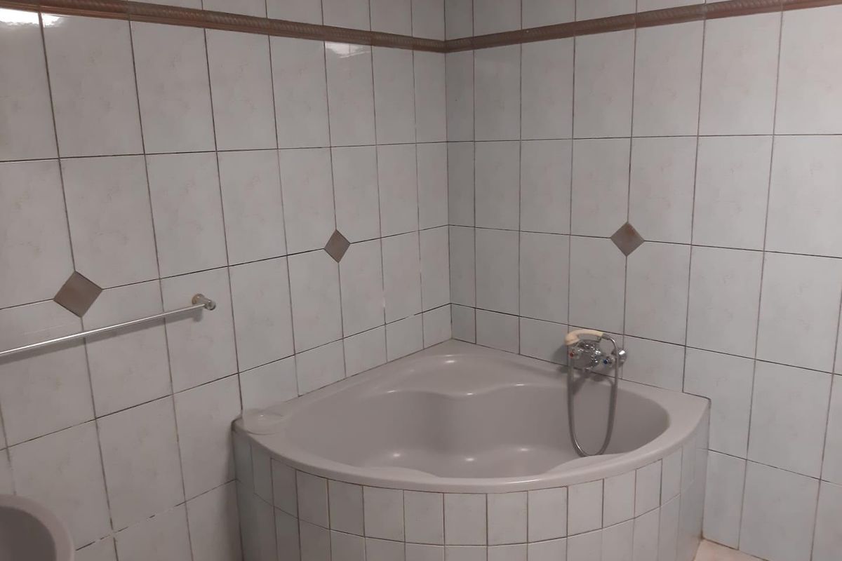 A dated bathroom featuring a corner bathtub with tiled surround and wall-mounted faucet, requiring cosmetic updates to modernize the space.