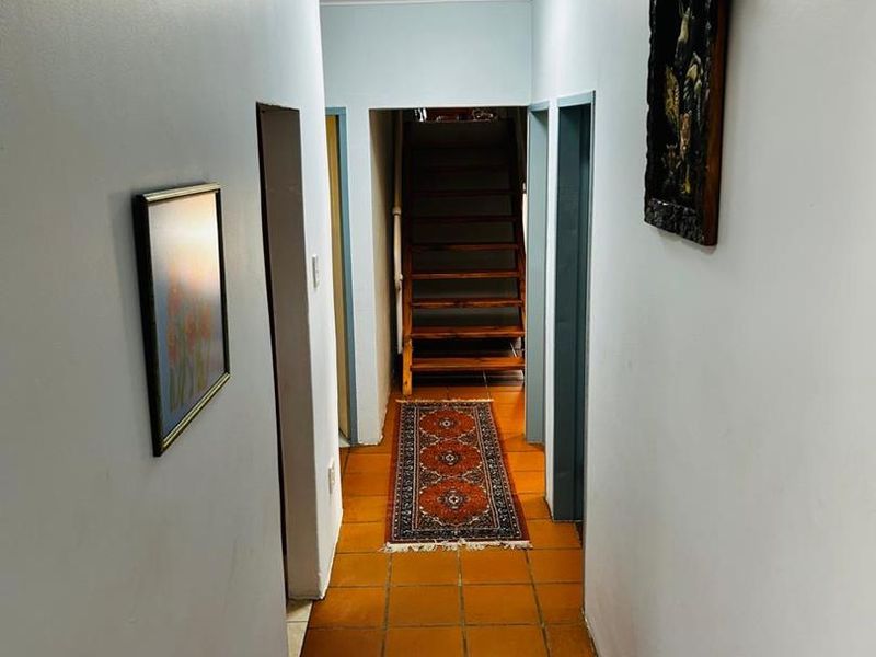 A functional hallway featuring terracotta floor tiles, crown molding, and a wooden staircase leading to the upper level.