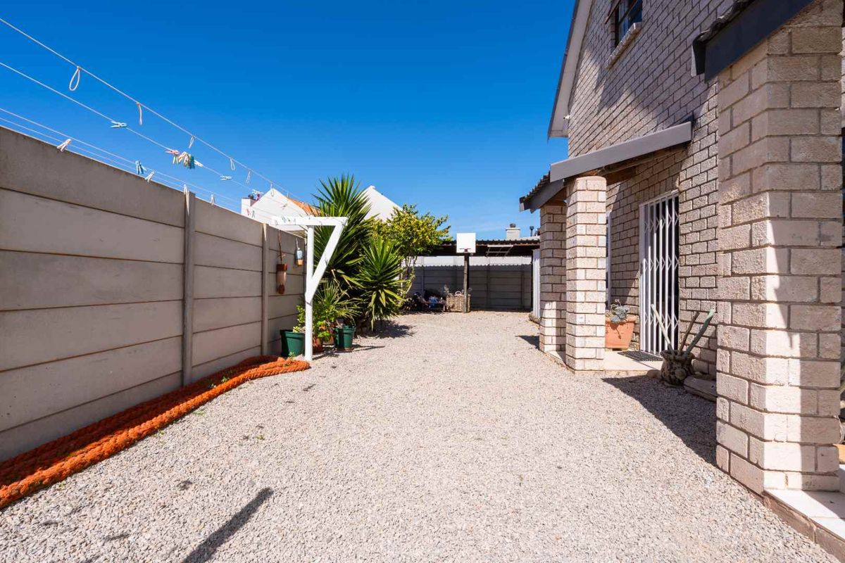 A rear exterior view featuring a gravel driveway, precast concrete boundary walls, and a brick-clad building facade with a security gate.