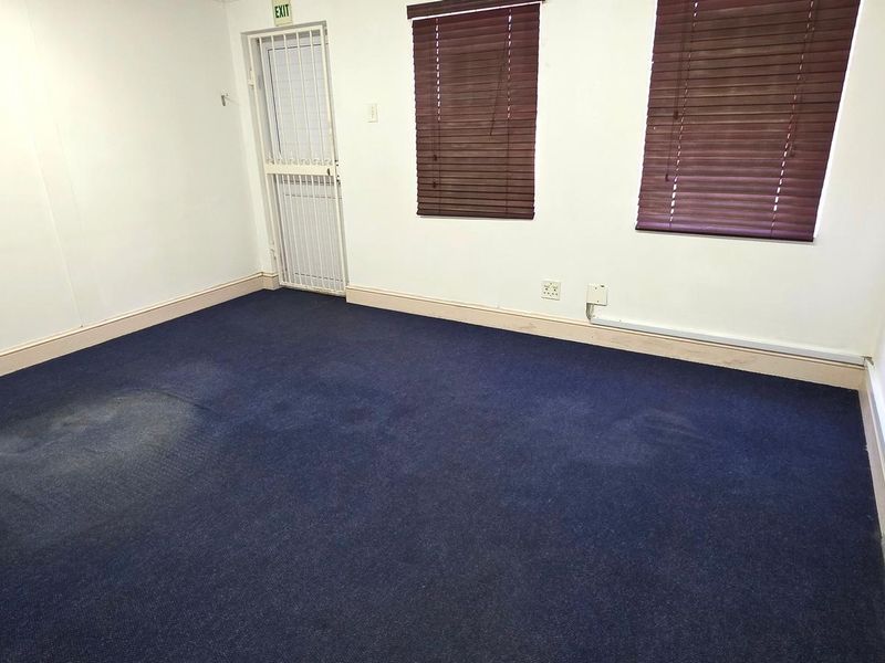 An empty office space featuring blue carpeting, security gate access, and window blinds, suitable for a professional workspace.