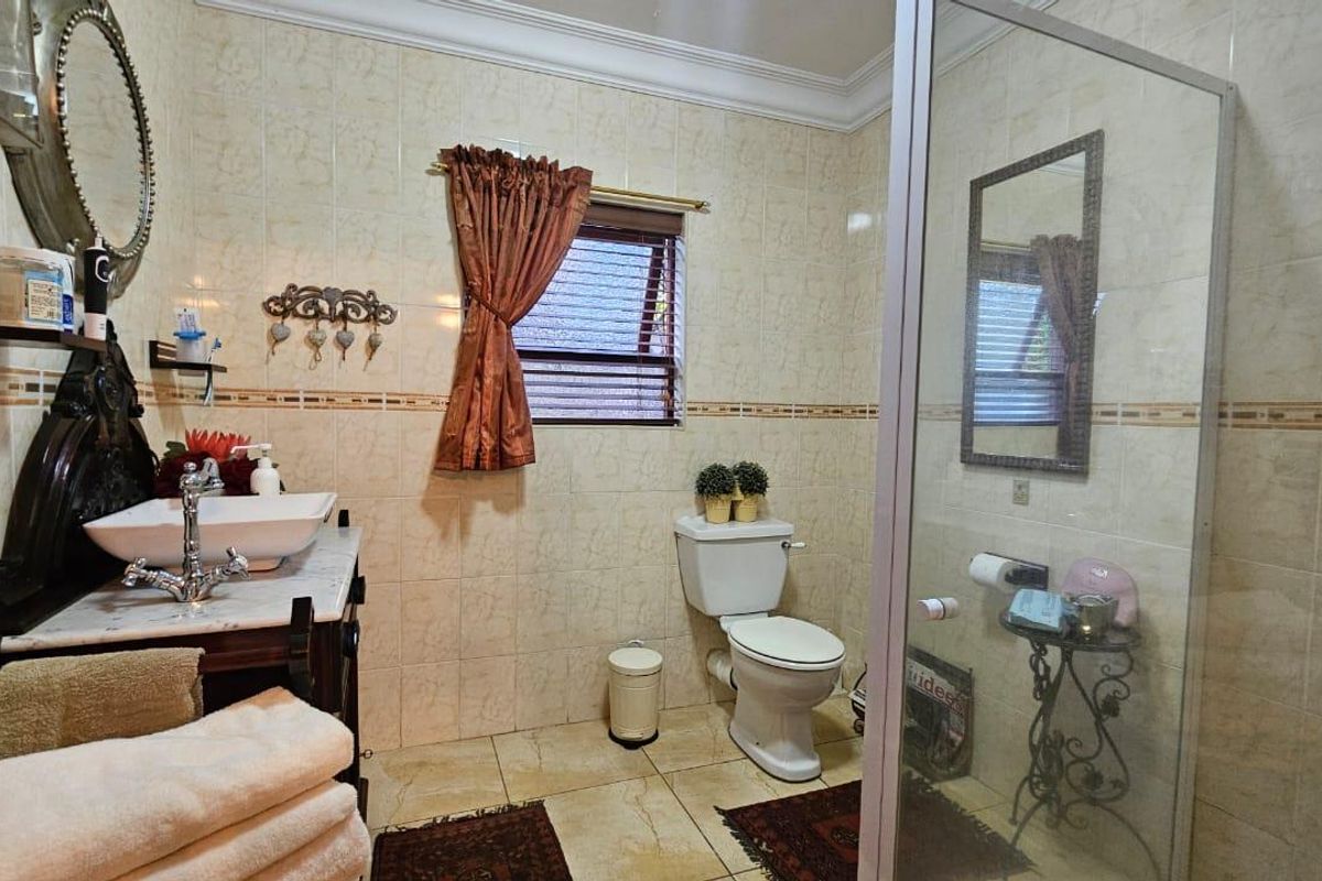 A functional bathroom featuring a vanity with a vessel sink, a toilet, and a glass-enclosed shower with floor-to-ceiling wall tiles.