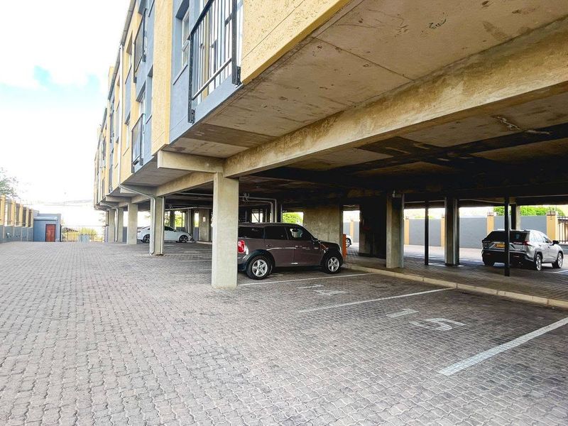 Covered ground-level parking area featuring concrete structural supports and paved surfacing beneath the apartment building.