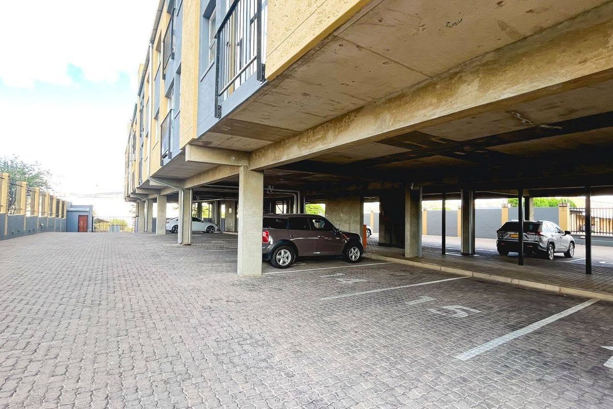 Covered ground-level parking area featuring concrete structural supports and paved surfacing beneath the apartment building.