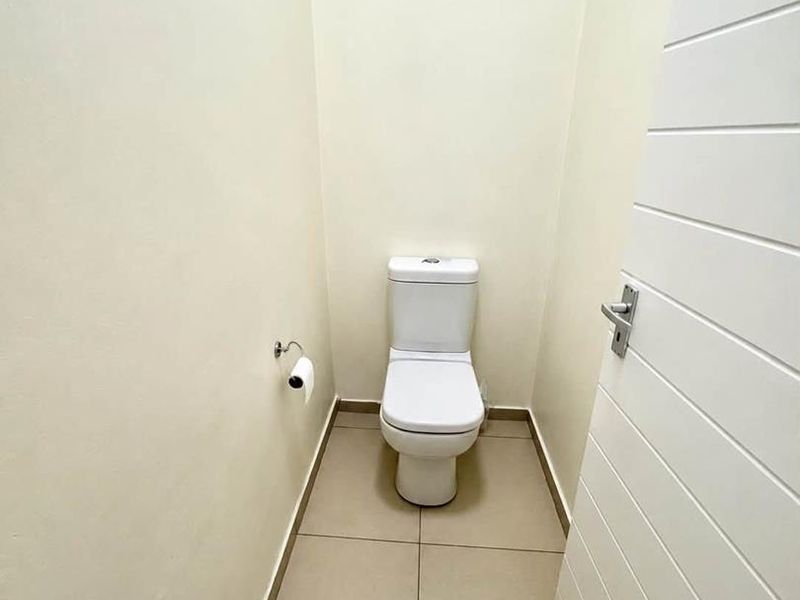A clean and minimalist guest toilet featuring neutral floor tiles and a modern white toilet suite.