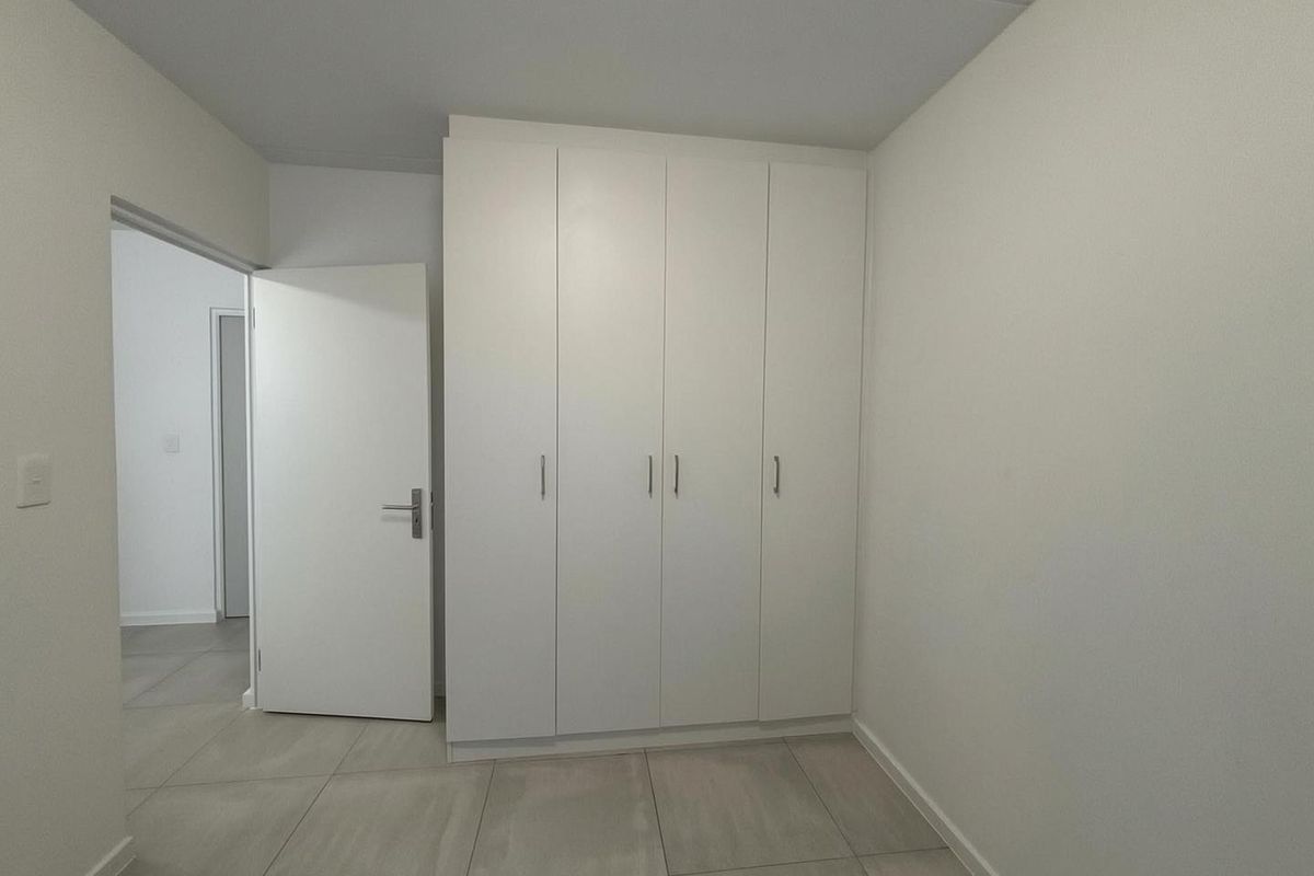 A clean, minimalist bedroom featuring neutral floor tiles and built-in white cabinetry with modern hardware.