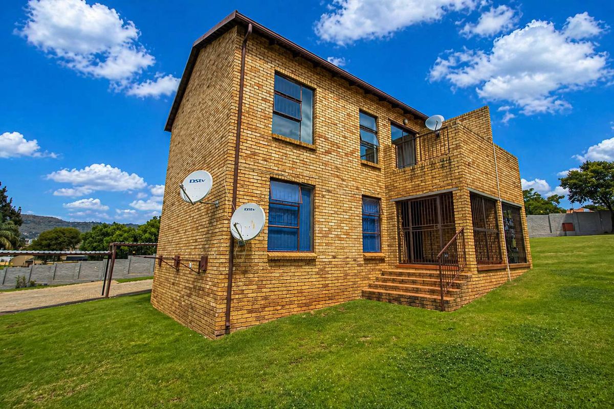 A two-story face-brick apartment building exterior featuring metal security gates, multiple satellite dishes, and a surrounding lawn area.