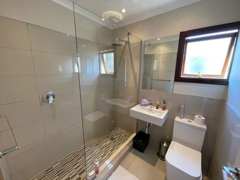 Modern bathroom featuring a glass-enclosed walk-in shower with rain shower head, wall-mounted basin, and tiled finishes throughout.