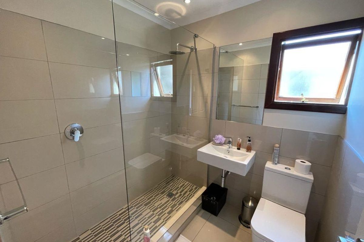 Modern bathroom featuring a glass-enclosed walk-in shower with rain shower head, wall-mounted basin, and tiled finishes throughout.