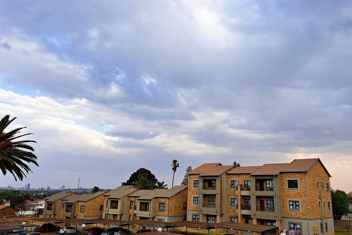 Exterior view of a multi-story apartment complex featuring face-brick facades, tiled roofs, and covered parking bays under a cloudy sky.