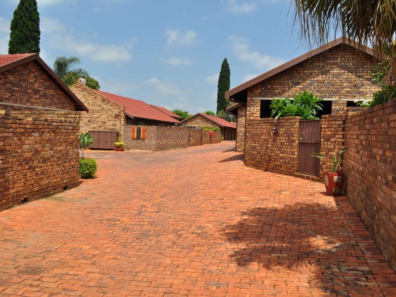 A view of the townhouse complex driveway featuring face-brick exterior walls, paved surfaces, and tiled roofing.