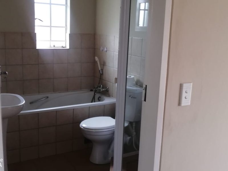A functional bathroom featuring a pedestal basin, bathtub with shower mixer, and a standard toilet with tiled splashback finishes.