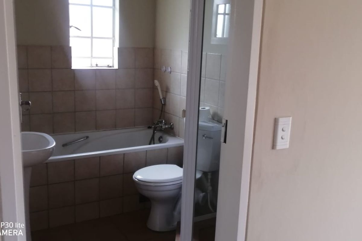 A functional bathroom featuring a pedestal basin, bathtub with shower mixer, and a standard toilet with tiled splashback finishes.