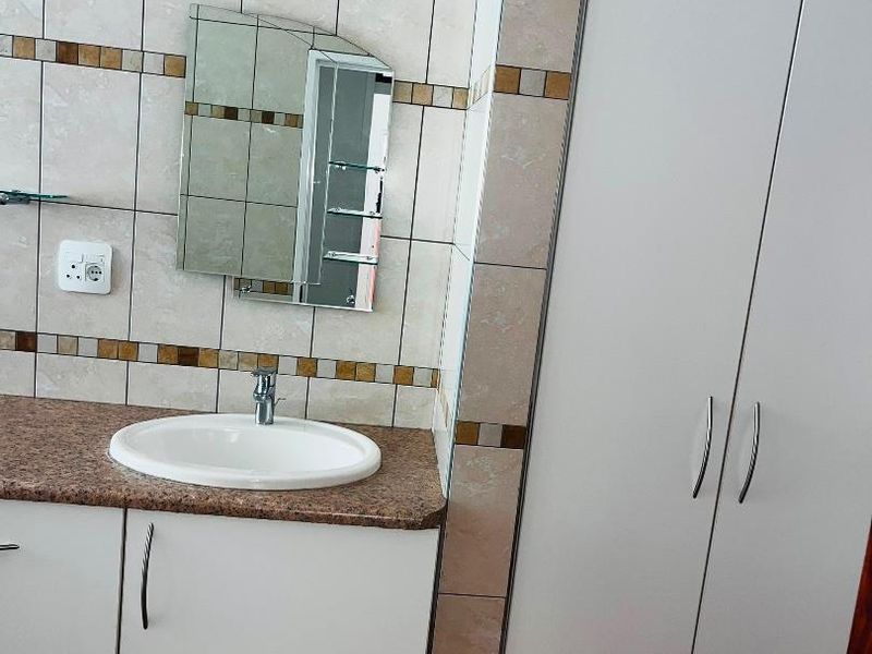 A functional bathroom featuring a vanity with a granite countertop, drop-in sink, wall mirror, and built-in storage cupboards with tiled wall finishes.