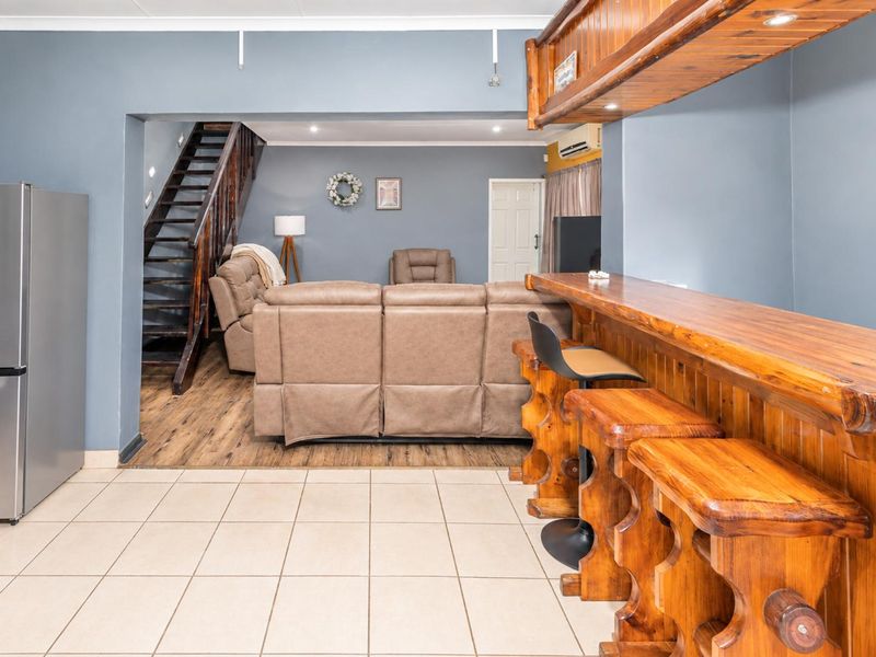 Open plan living area featuring a built-in wooden bar, tiled and laminate flooring, and a staircase leading to the upper level.