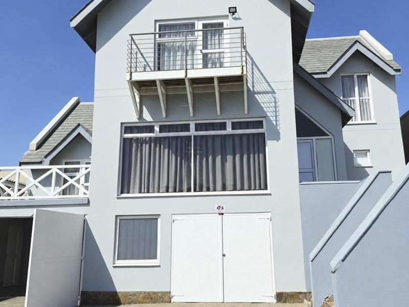 Front elevation of a multi-story house featuring a paved driveway, double garage, and an upper-level balcony with a metal railing.