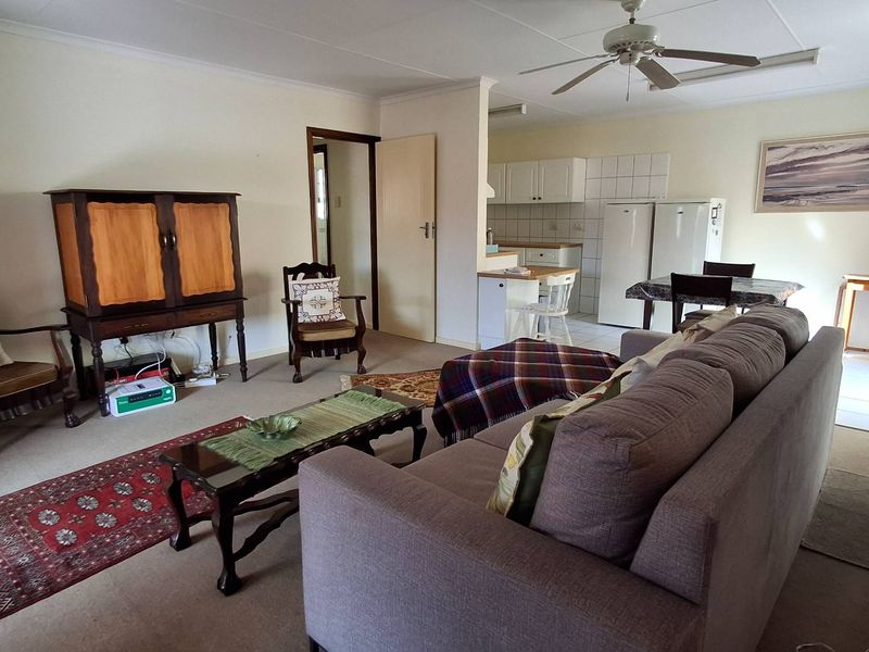 An open-plan living and kitchen area featuring a carpeted lounge, ceiling fan, and a functional kitchen with tiled flooring and cabinetry.
