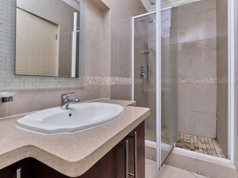 A clean, modern bathroom featuring a vanity with basin, wall-mounted mirror, and a glass-enclosed shower with tiled finishes.