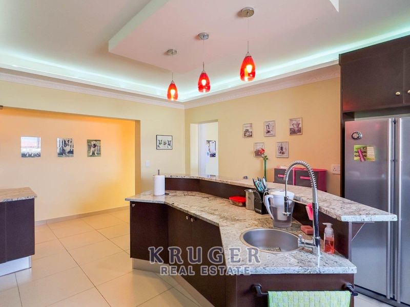 Spacious kitchen featuring dark cabinetry, granite countertops, a central island with a sink, and modern recessed and pendant lighting.