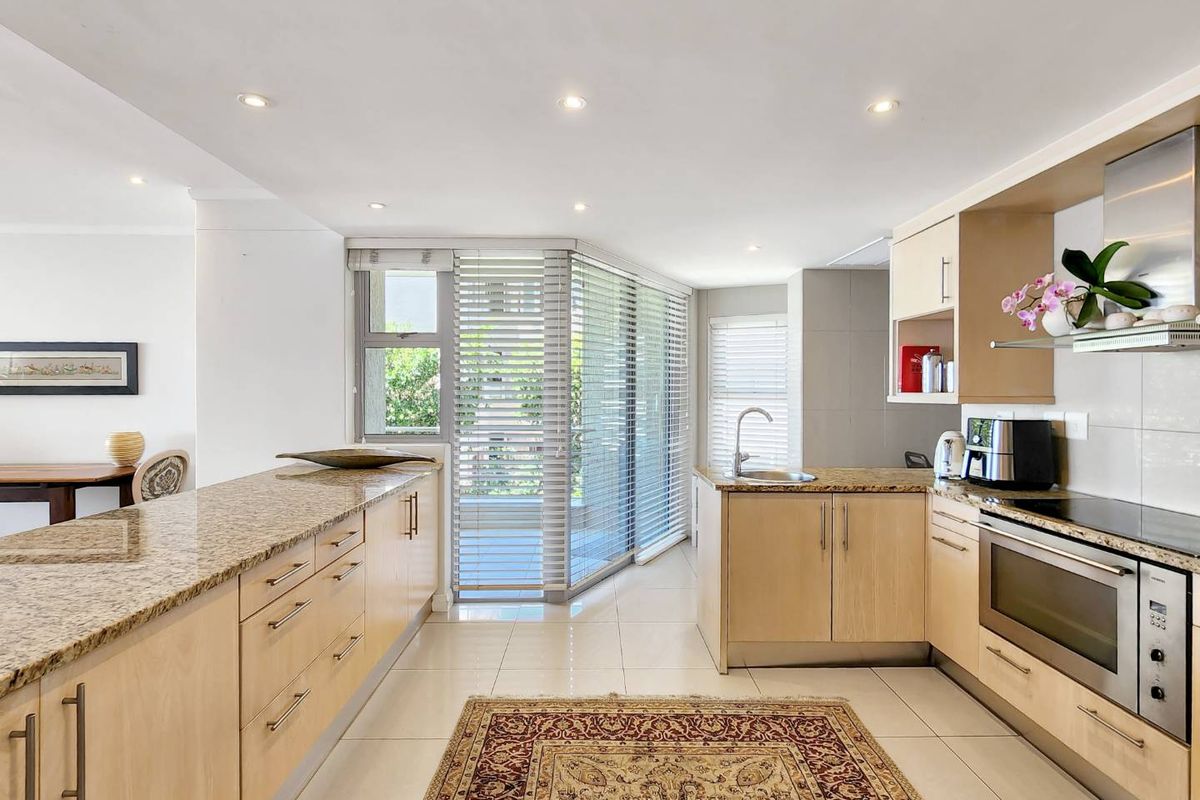 Modern kitchen featuring light wood cabinetry, granite countertops, integrated appliances, and large windows with blinds, creating a bright and functional cooking space.