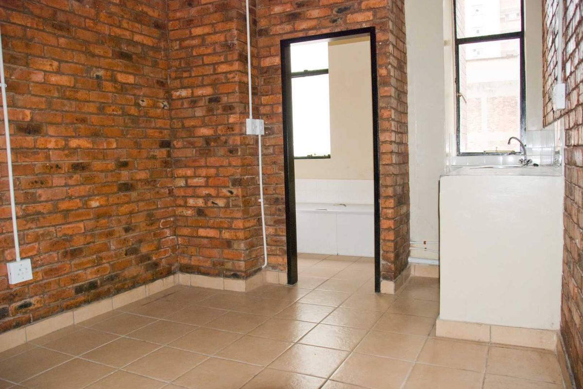 An empty kitchen area featuring exposed brick walls, tiled flooring, and a basic sink unit, offering a blank canvas for renovation.