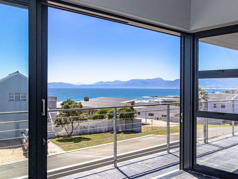 A bright interior space featuring large sliding glass doors that open onto a balcony with expansive coastal and mountain views.