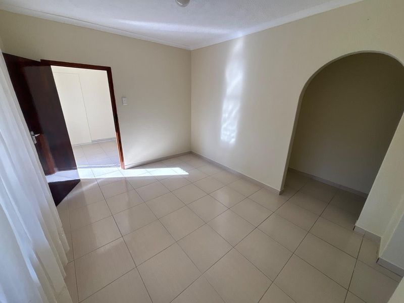 An empty bedroom featuring neutral tiled flooring, a decorative archway, and clean wall finishes, offering a versatile space ready for personalization.