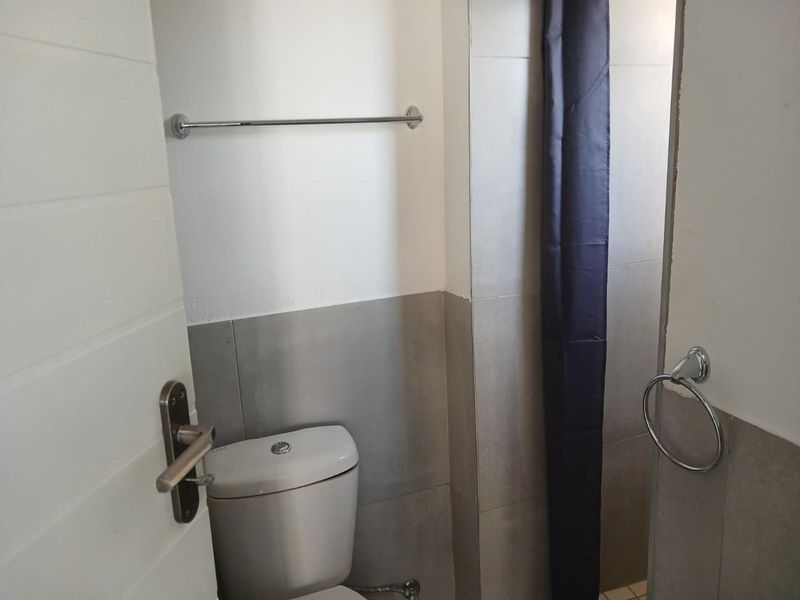 A compact bathroom featuring neutral wall tiling, a standard toilet, and chrome bathroom accessories.