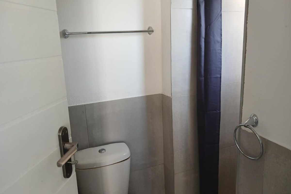 A compact bathroom featuring neutral wall tiling, a standard toilet, and chrome bathroom accessories.