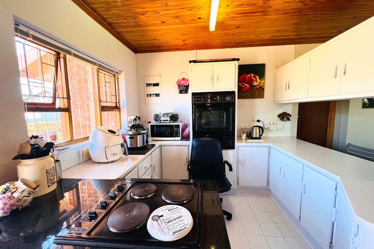 A functional kitchen featuring built-in cabinetry, an integrated oven, electric hob, and a distinctive timber-paneled ceiling with tiled flooring.