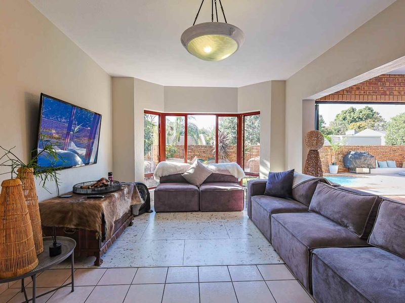 Spacious living room featuring large bay windows, terrazzo-style flooring, and direct access to the outdoor patio and pool area.