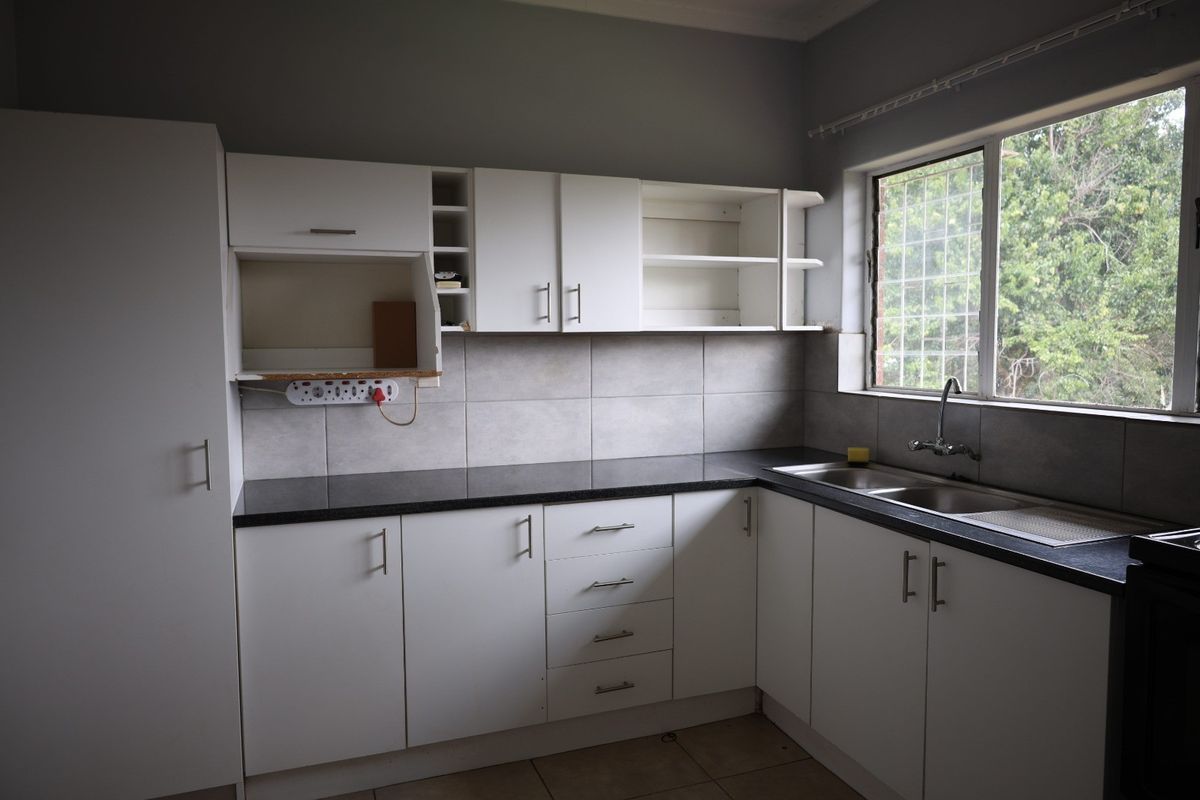 A functional kitchen featuring white built-in cabinetry, dark countertops, a double basin sink, and tiled backsplash, offering a clean canvas for potential updates.