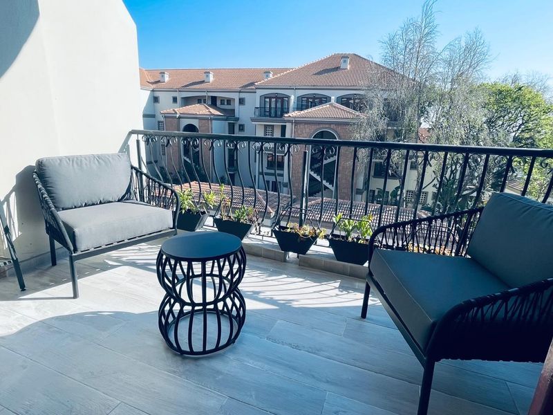 A well-maintained apartment balcony featuring a decorative wrought iron balustrade and tiled flooring, offering an elevated view of the surrounding complex.