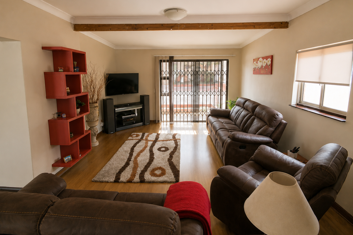 A comfortable living room featuring laminate flooring, an exposed timber ceiling beam, and a sliding glass door with a security gate leading outdoors.