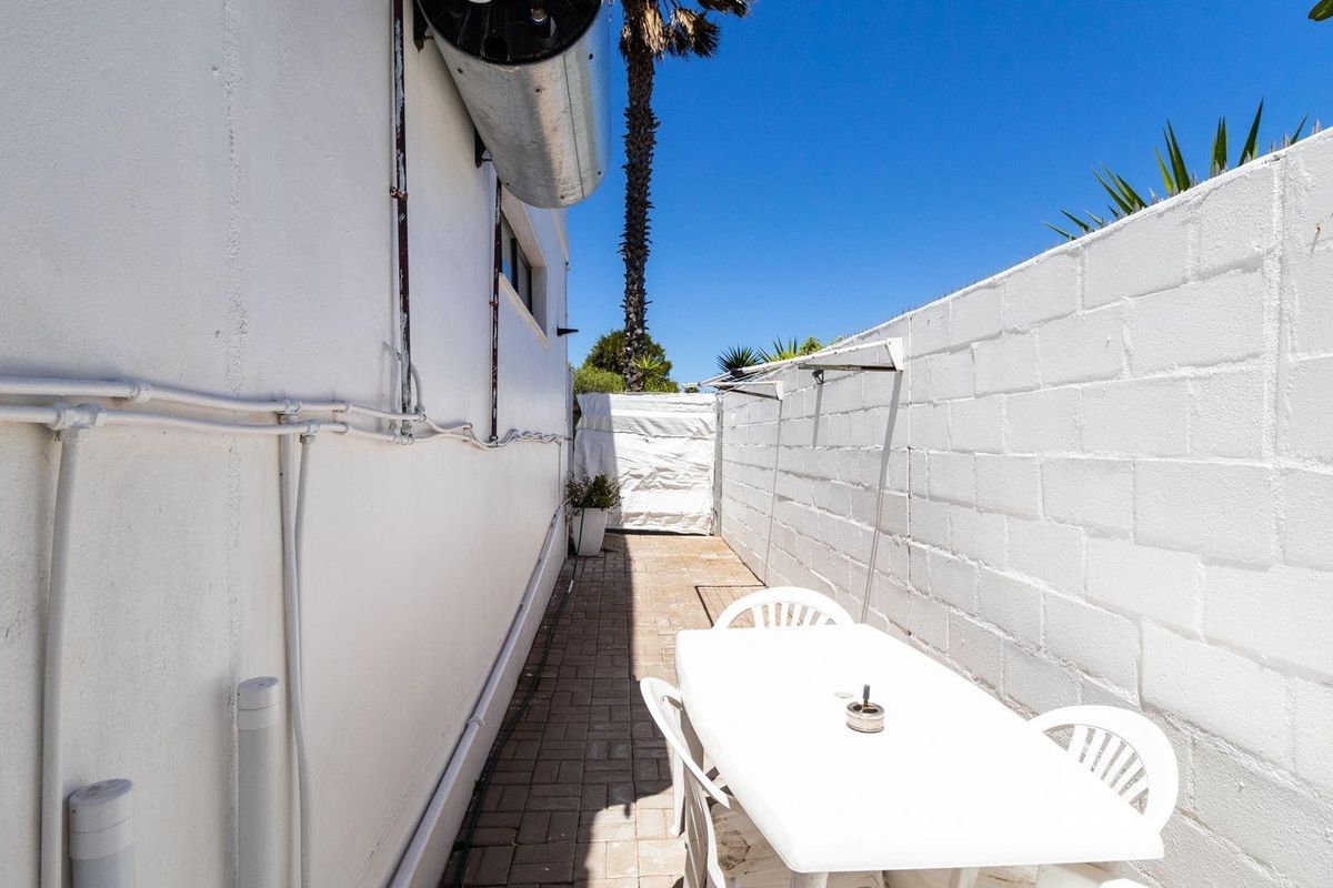 A narrow exterior side passage featuring paved flooring, a boundary wall, and an externally mounted water heater unit.
