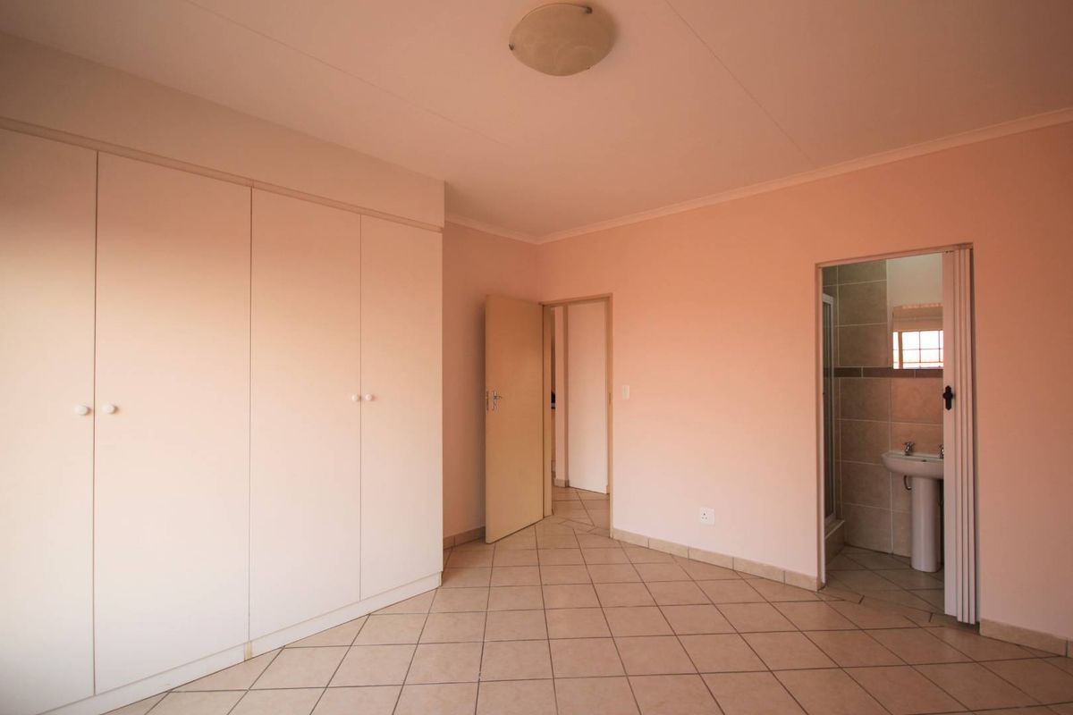 A spacious, empty bedroom featuring neutral tiled flooring, built-in cupboards, and direct access to an en-suite bathroom.