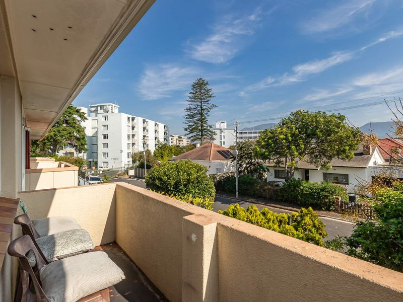 A private balcony featuring a concrete balustrade and tiled flooring, offering an elevated view of the surrounding neighborhood and streetscape.