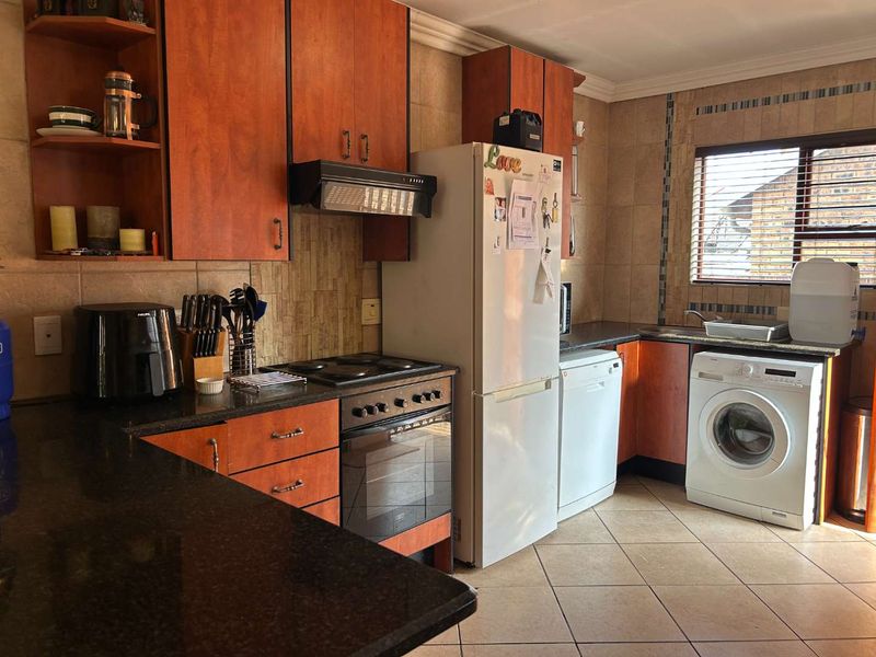 Functional kitchen featuring warm-toned cabinetry, granite countertops, integrated stove and oven, tiled backsplash, and dedicated space for laundry appliances.