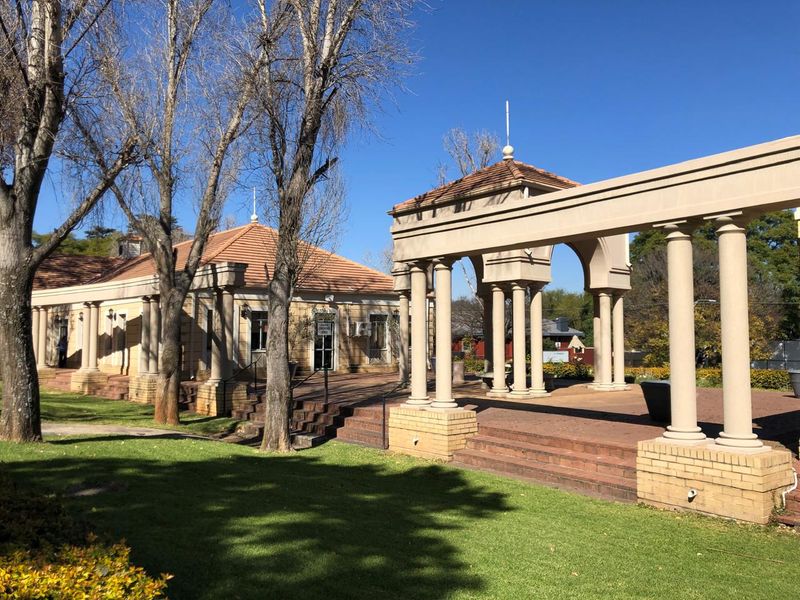 A well-maintained office exterior featuring a spacious brick patio, classical columns, and a pergola structure set within a landscaped garden area.