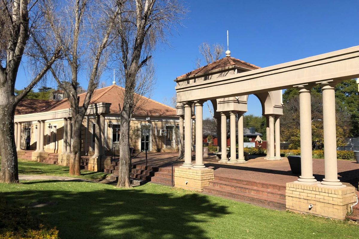 A well-maintained office exterior featuring a spacious brick patio, classical columns, and a pergola structure set within a landscaped garden area.