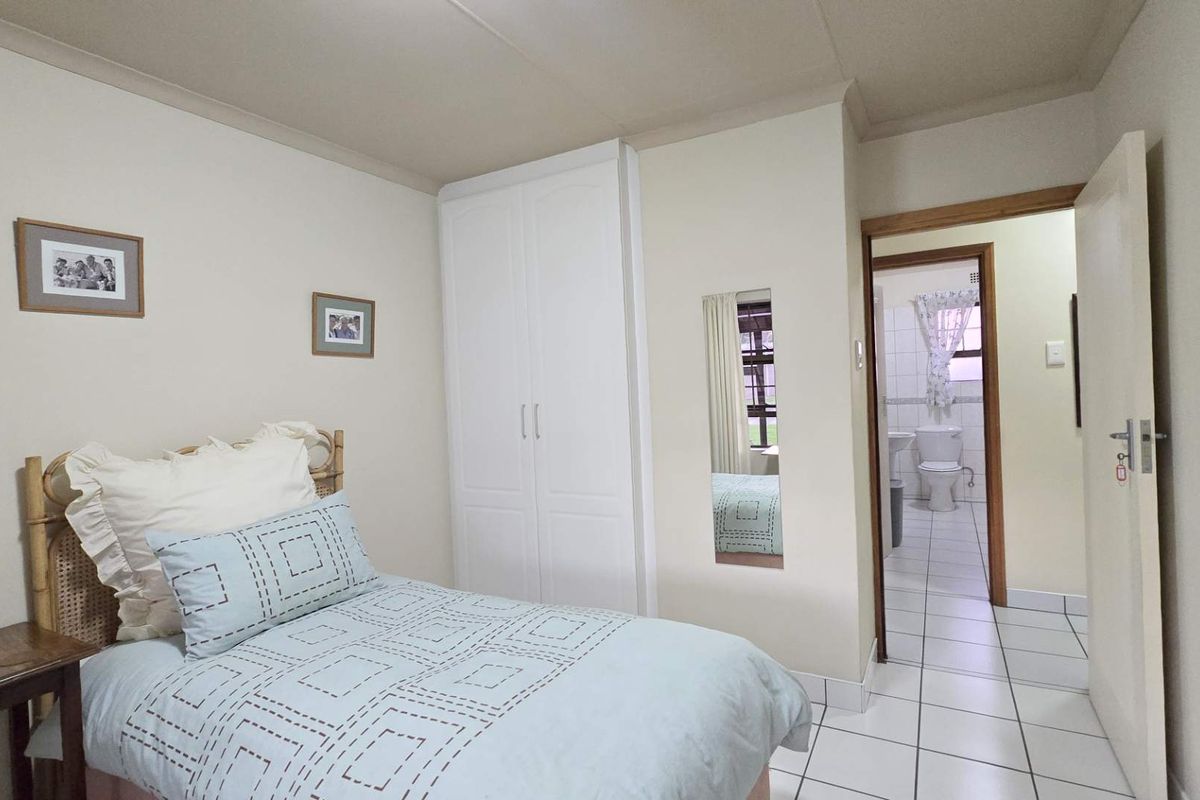 A bedroom featuring built-in cupboards and tiled flooring, with an adjoining en-suite bathroom visible through the doorway.