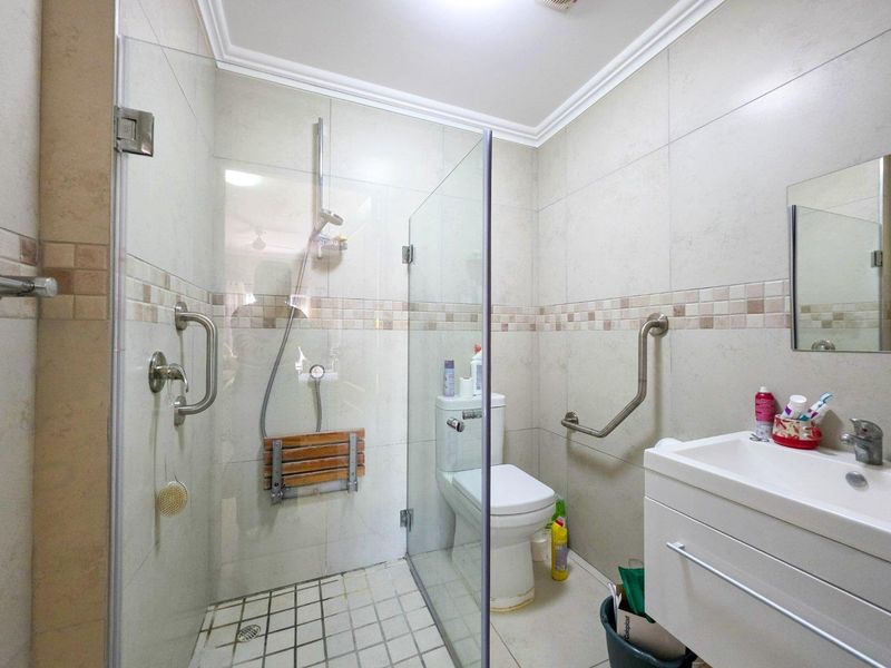 Functional bathroom featuring a walk-in shower with glass screen, fold-down seat, safety grab rails, and a modern vanity basin.