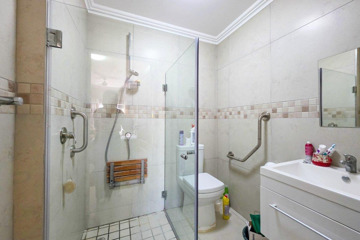 Functional bathroom featuring a walk-in shower with glass screen, fold-down seat, safety grab rails, and a modern vanity basin.
