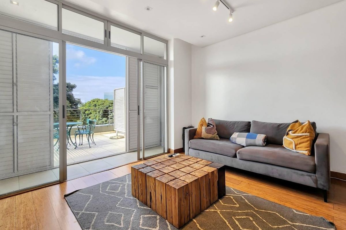 Bright living room featuring hardwood flooring and large sliding glass doors that provide seamless access to an outdoor balcony area.