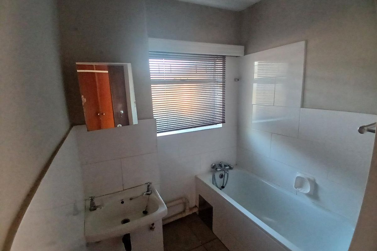 A functional bathroom featuring a bathtub, wall-mounted basin, and tiled splashback, currently in need of cosmetic updates and modernization.