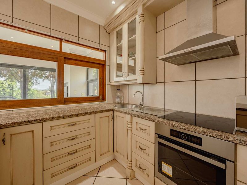 A well-maintained kitchen featuring granite countertops, built-in oven, electric hob, stainless steel extractor fan, and classic cabinetry with tiled splashbacks.