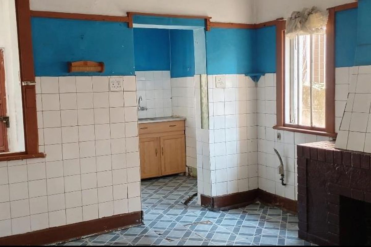 A dated kitchen area featuring a brick fireplace, tiled walls, and original timber window frames, requiring significant renovation and modernization.