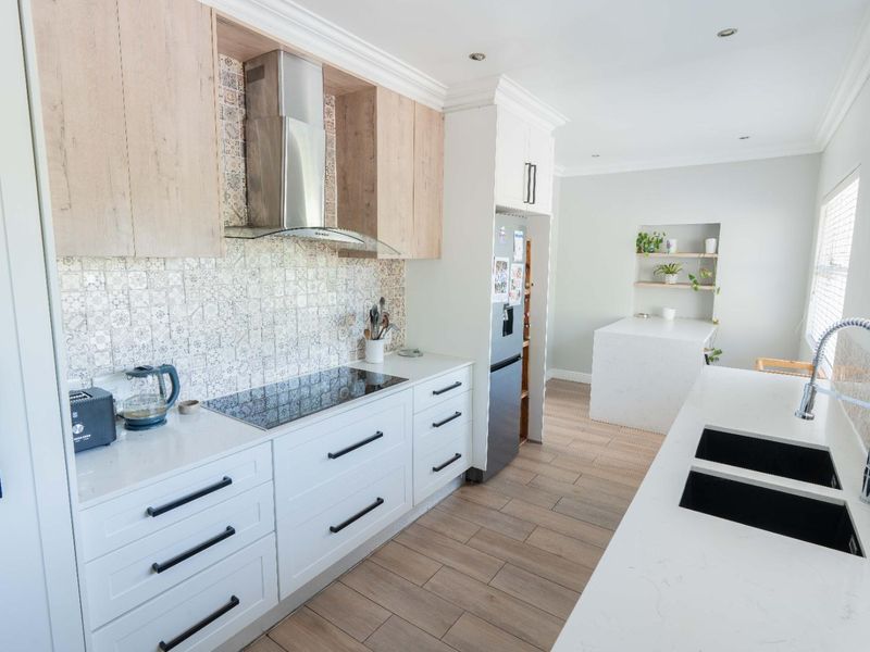 Modern kitchen featuring light wood and white cabinetry, stone countertops, induction hob, extractor fan, and a double undermount sink with a gooseneck faucet.