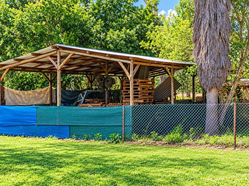 An outdoor utility structure featuring a timber frame and corrugated metal roof, enclosed by chain link fencing and temporary shade cloth screening.