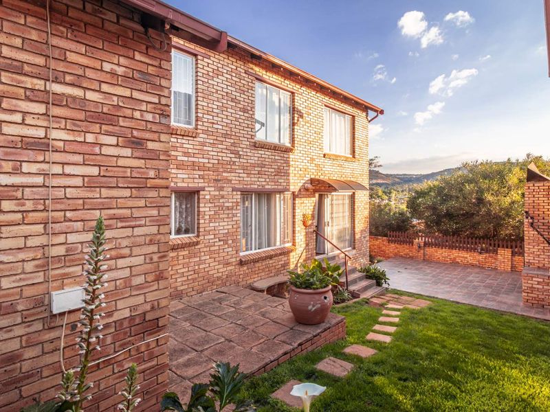 Rear view of the townhouse featuring a face brick facade, paved patio area, built-in braai, and a well-maintained garden.