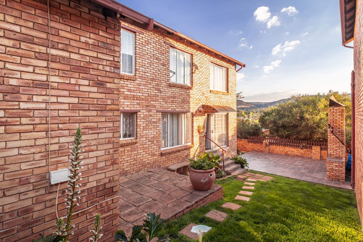 Rear view of the townhouse featuring a face brick facade, paved patio area, built-in braai, and a well-maintained garden.